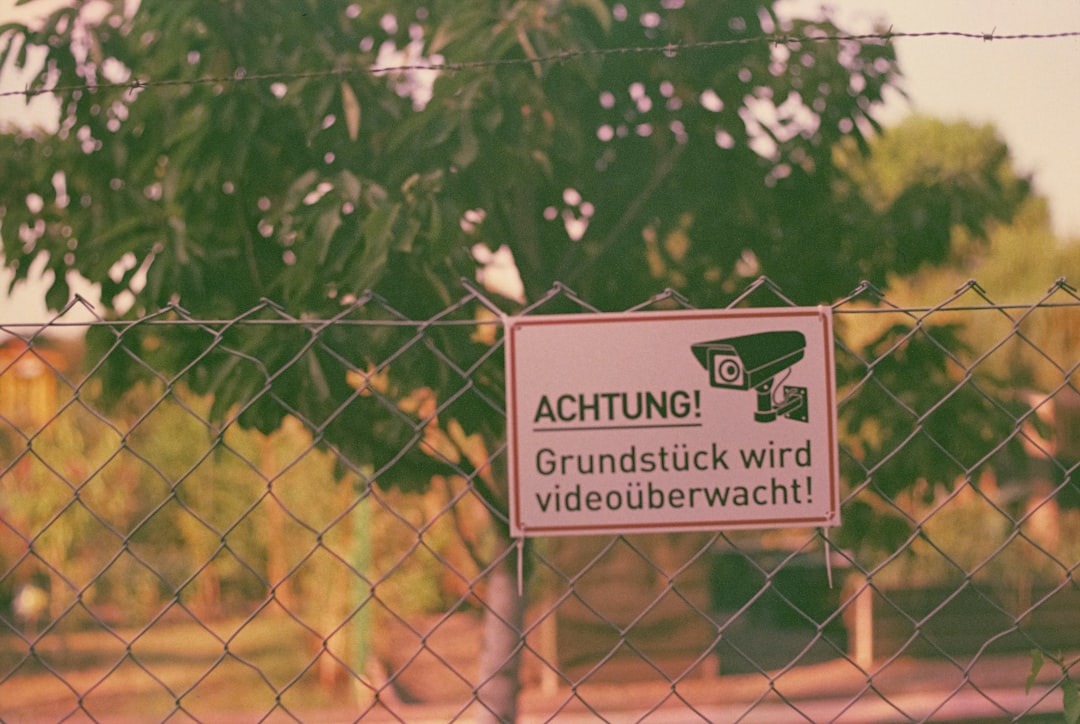 Warning sign with surveillance camera icon on chain-link fence.