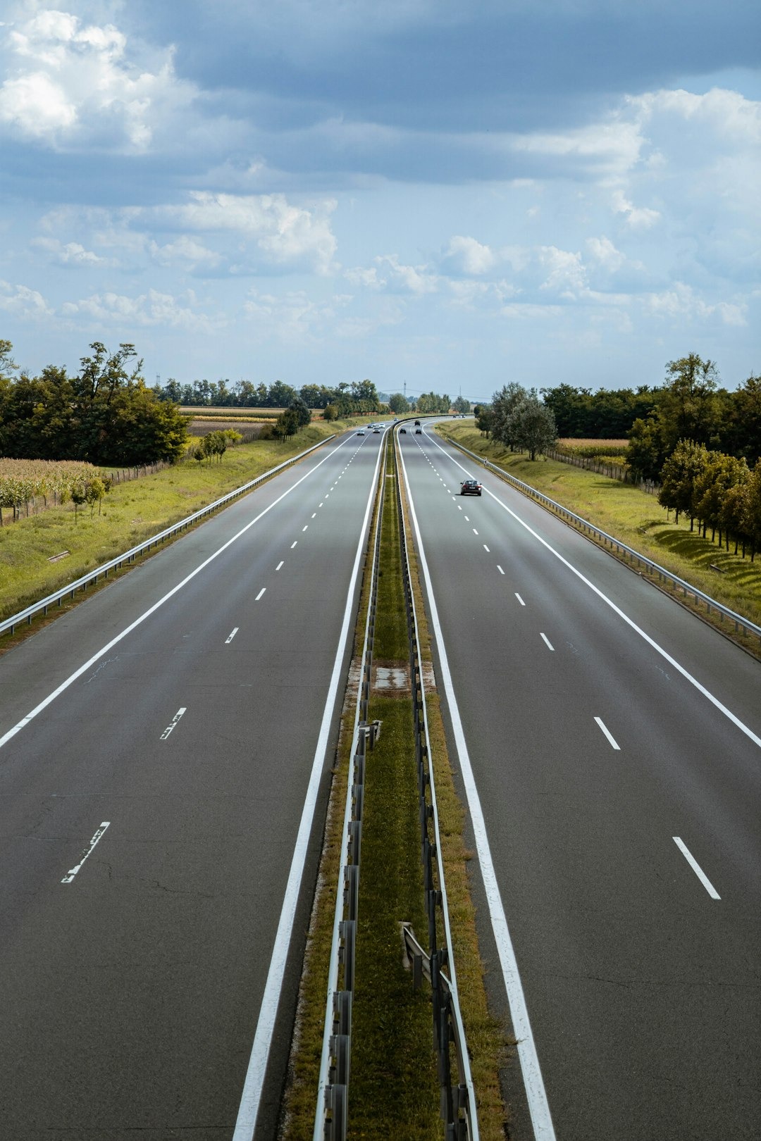 Multi-lane highway leading to the horizon through green fields.