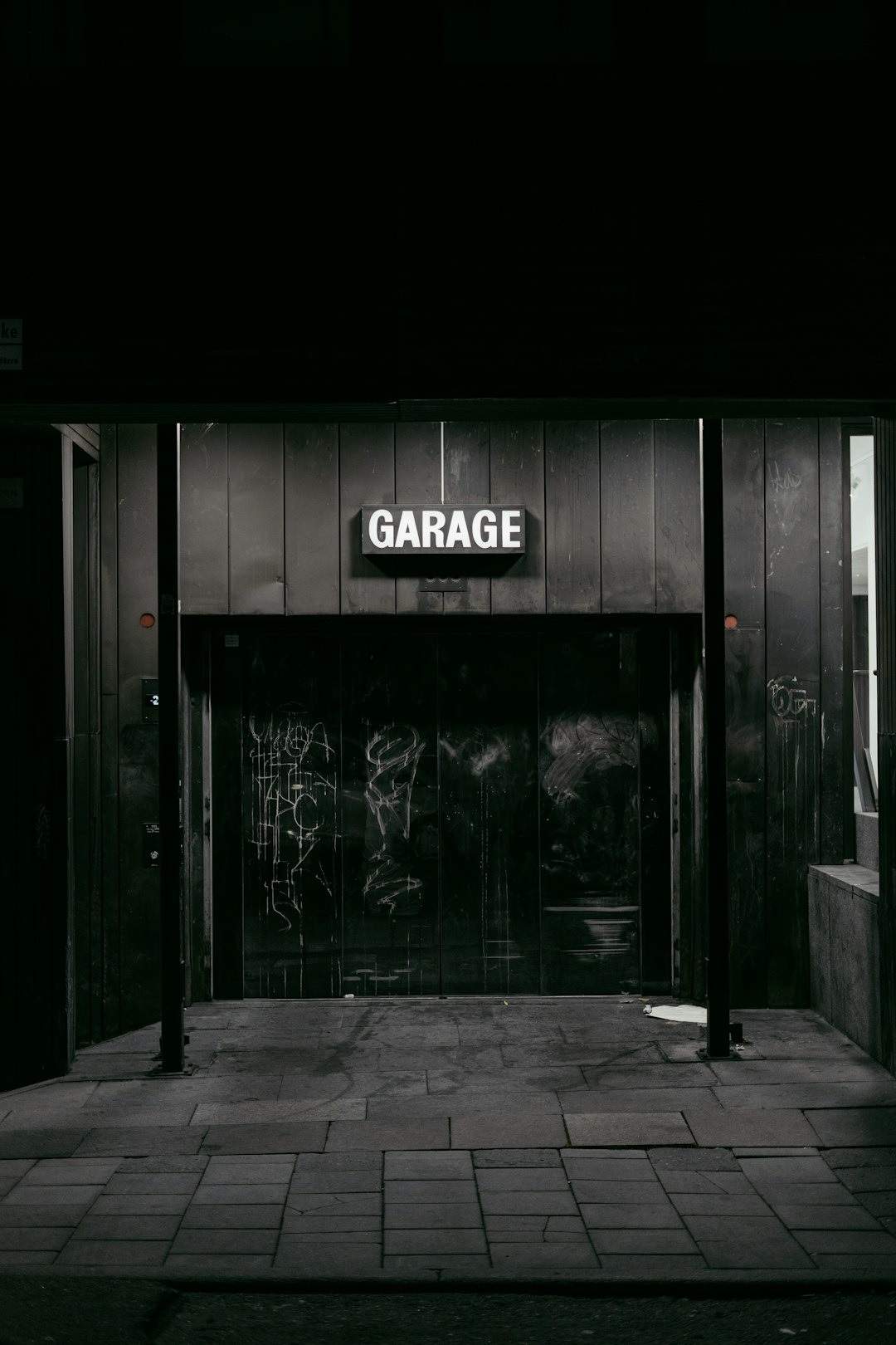 An illuminated garage sign above graffiti covered metal doors.